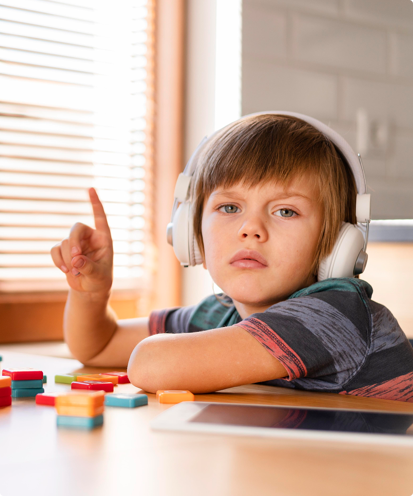 Bambino con le cuffie seduto al tavolo con tessere colorate