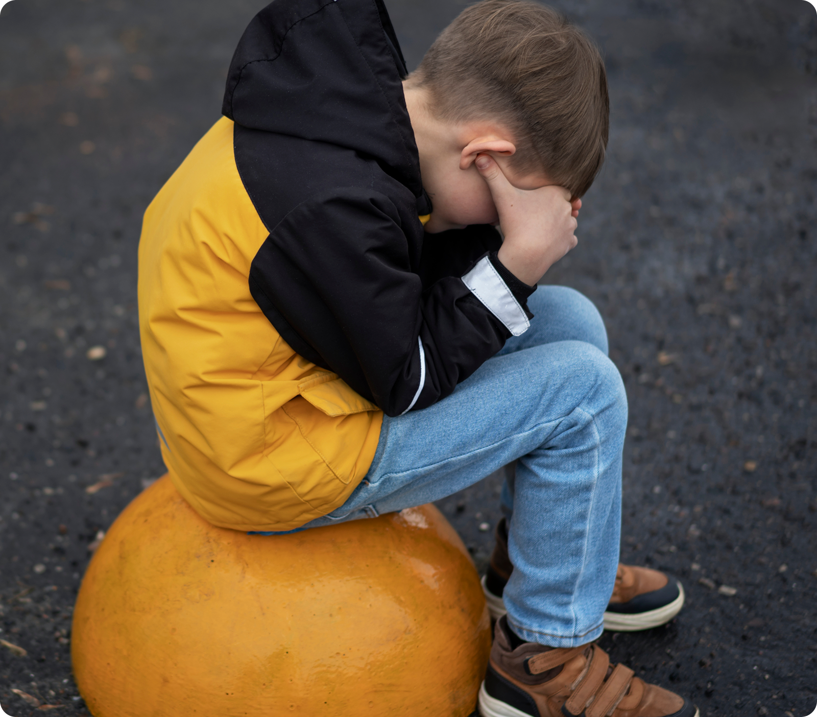 Bambino con giacca gialla seduto, che si copre il viso